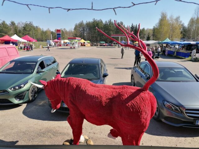 Etualalla rengon punainen härkä puuveistos, sen takana rivi autoja ja niiden takana markkina-alue